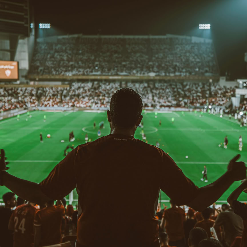 Excited fans watch a thrilling football match at a packed stadium under bright lights.